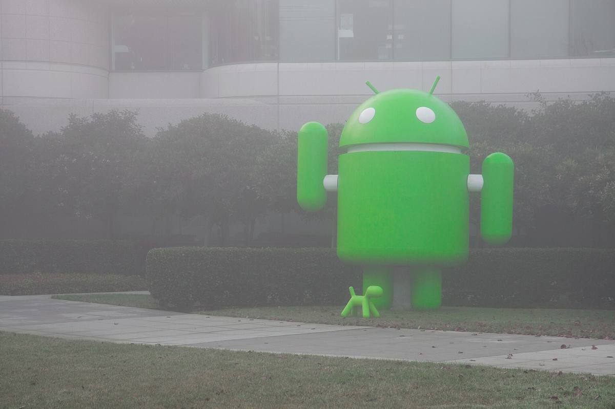 Zelená socha maskota Androidu v mlze před kancelářskou budovou
