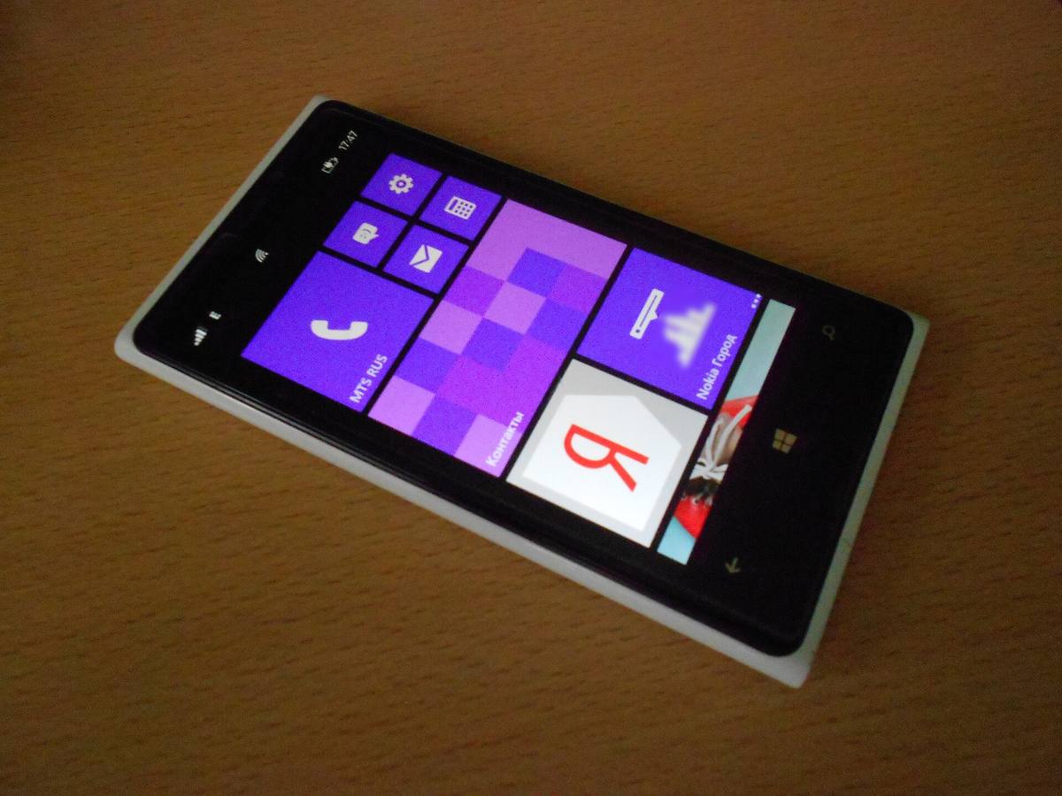 Bílý telefon Nokia Lumia 920 s dlaždicemi Windows Phone leží na dřevěném stole
