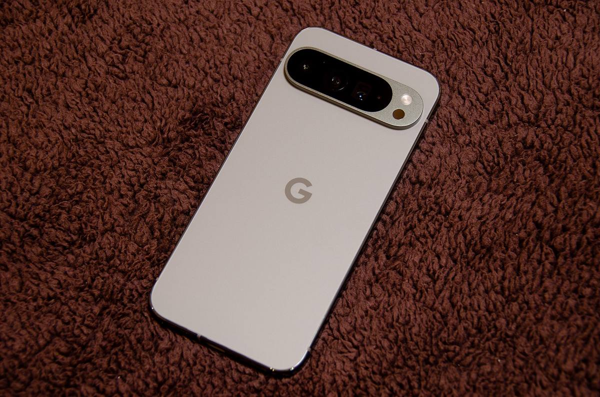 Zadní strana světlého telefonu Google Pixel 9 Pro XL s vodorovnou lištou fotoaparátů, položeného na hnědé dece