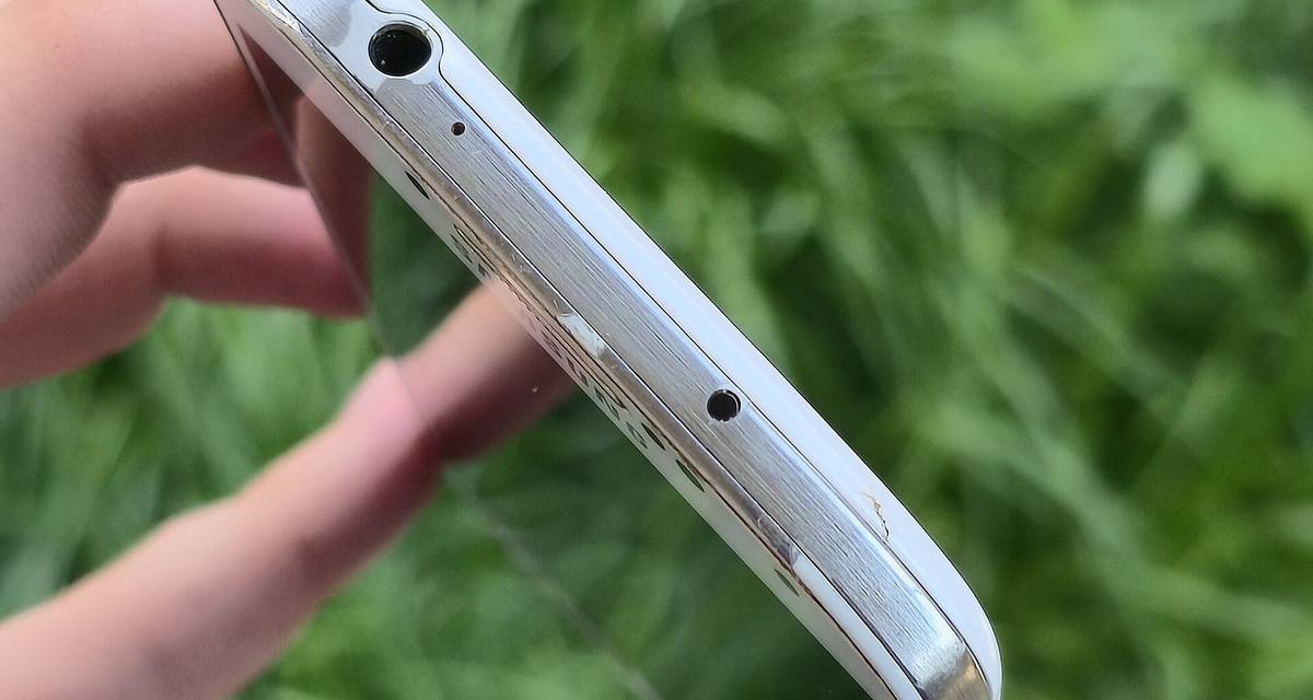 Horní hrana Samsungu Galaxy S4 držená v ruce, s konektorem sluchátek a mikrofonem