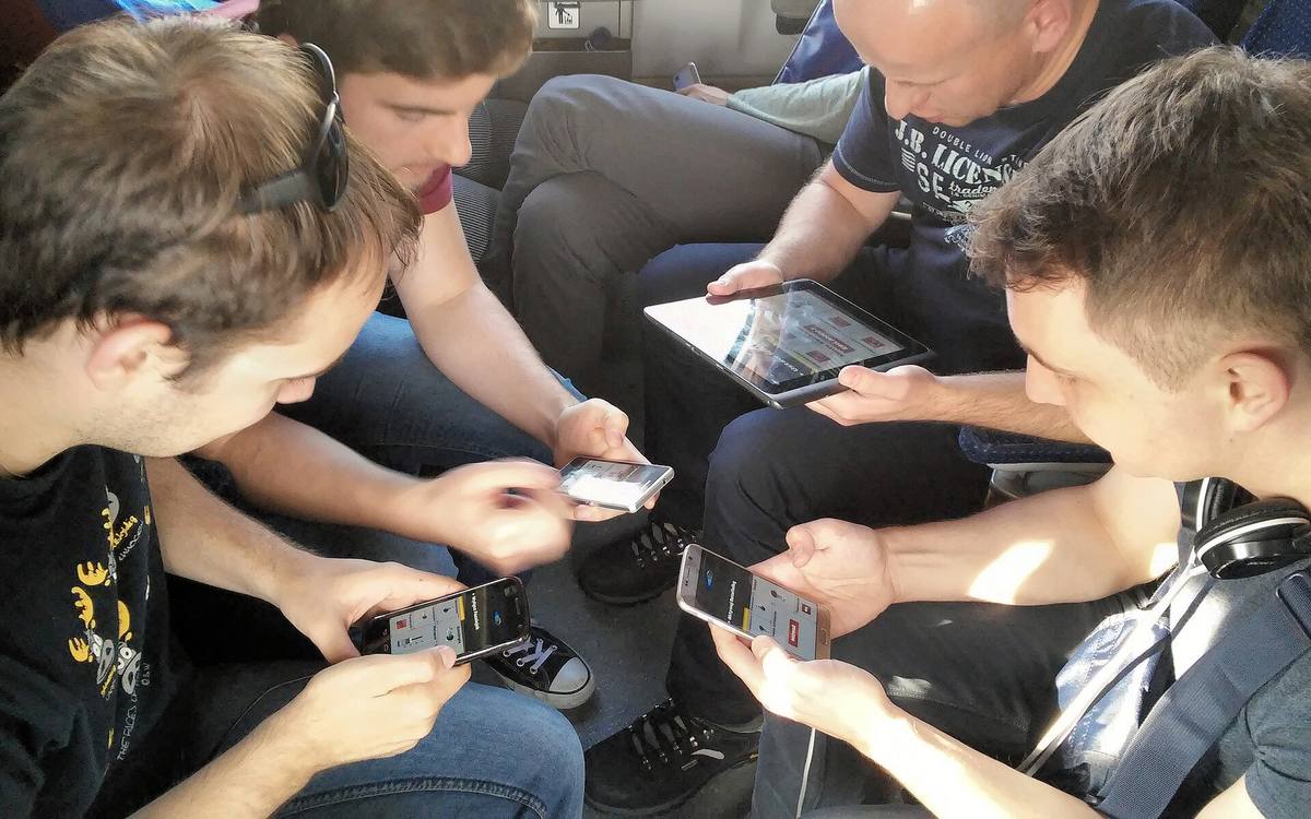 Čtyři lidé drží mobilní telefony a hrají tutéž hru