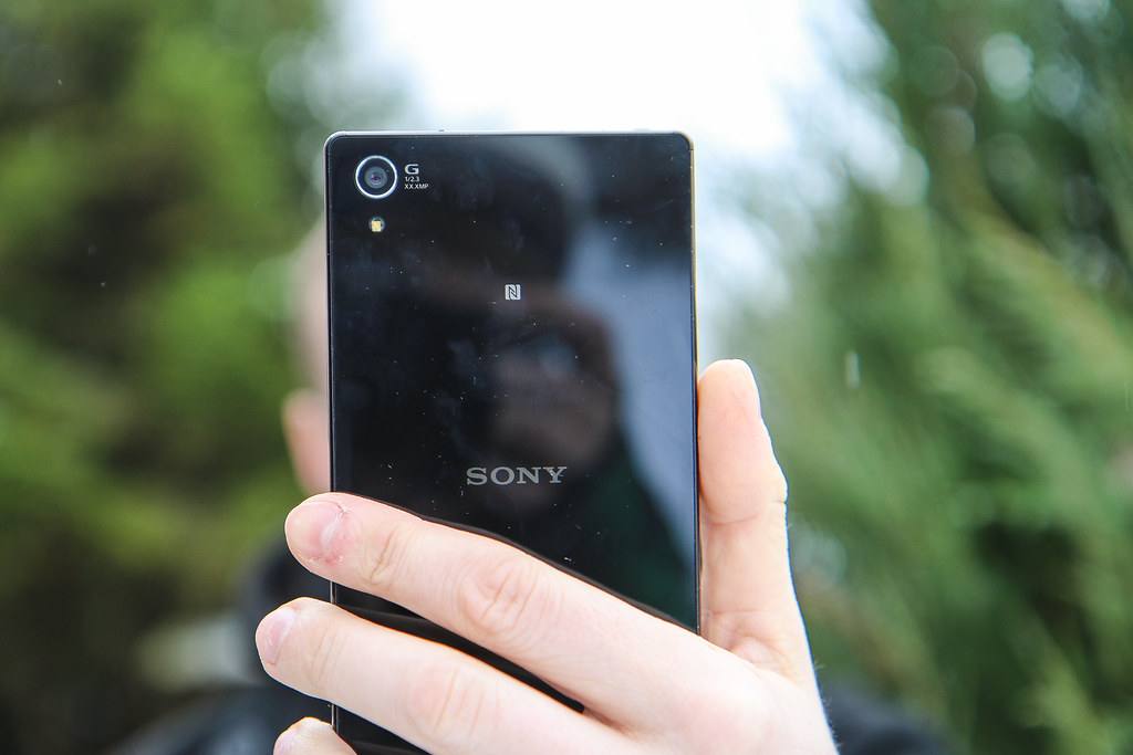 Zadní strana černého telefonu Sony drženého v ruce před zelení