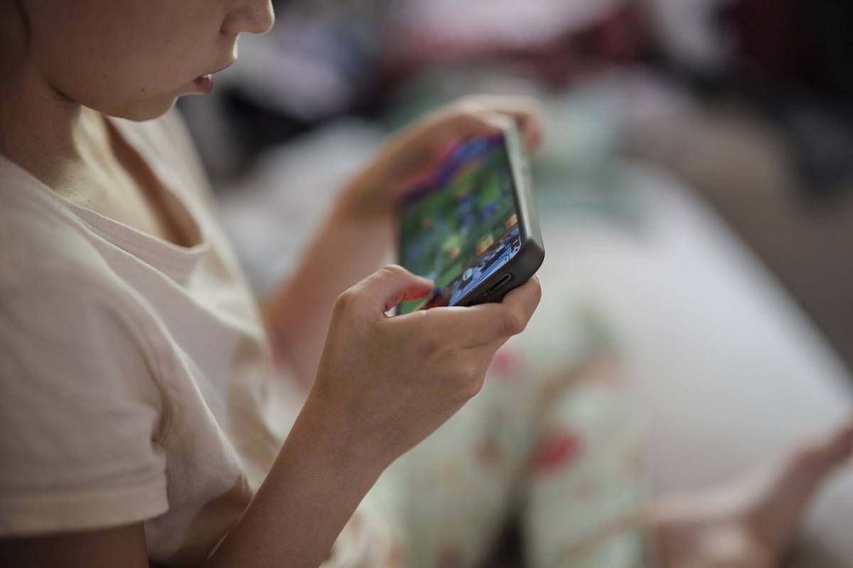 Dítě sedí doma na posteli a dívá se do telefonu