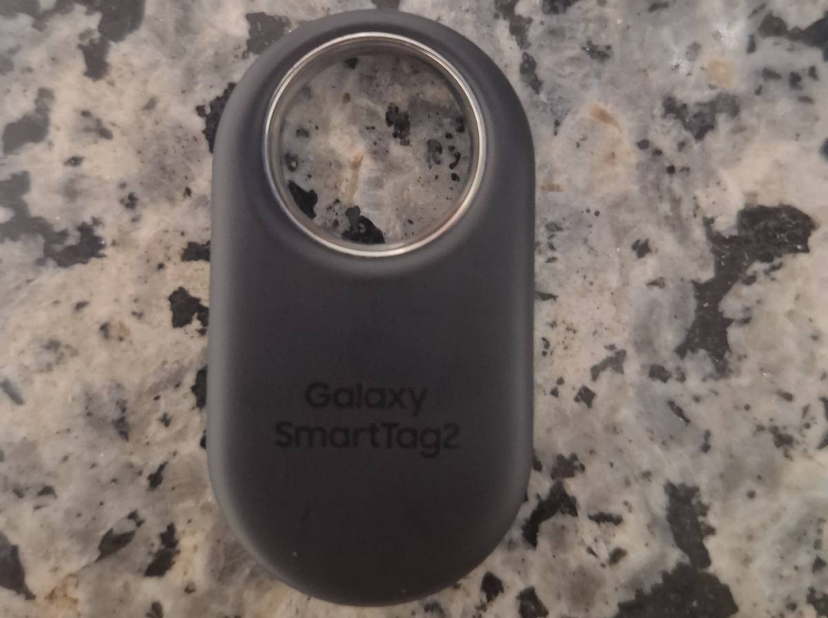 Černý přívěsek Galaxy SmartTag2 s kovovým očkem položený na žulové desce
