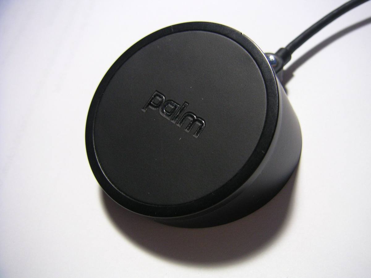 Černý kruhový nabíjecí dok Palm Touchstone s kabelem, ležící na bílé podložce