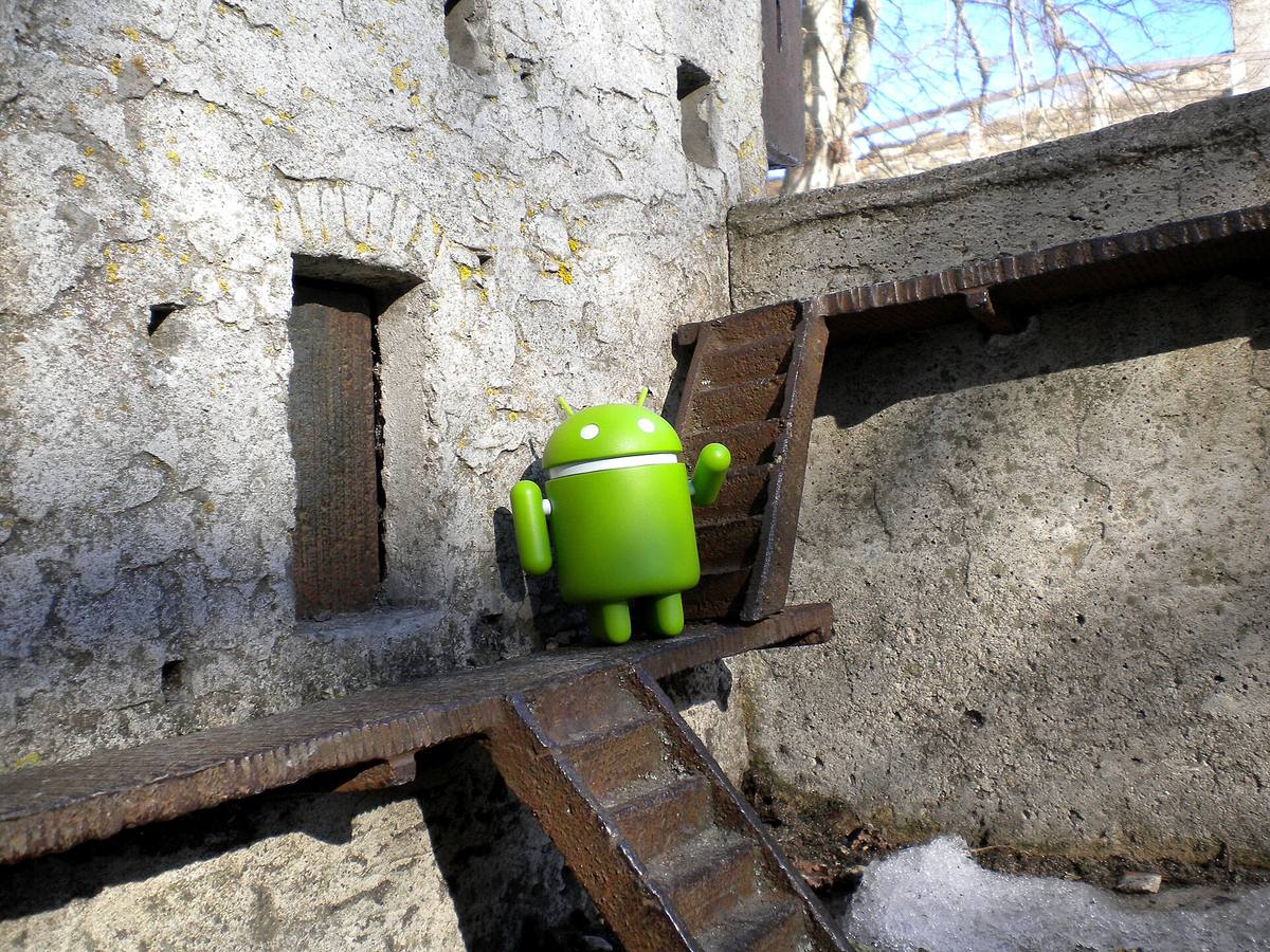 Zelená socha robota Androida stojí na trávníku před nízkou budovou