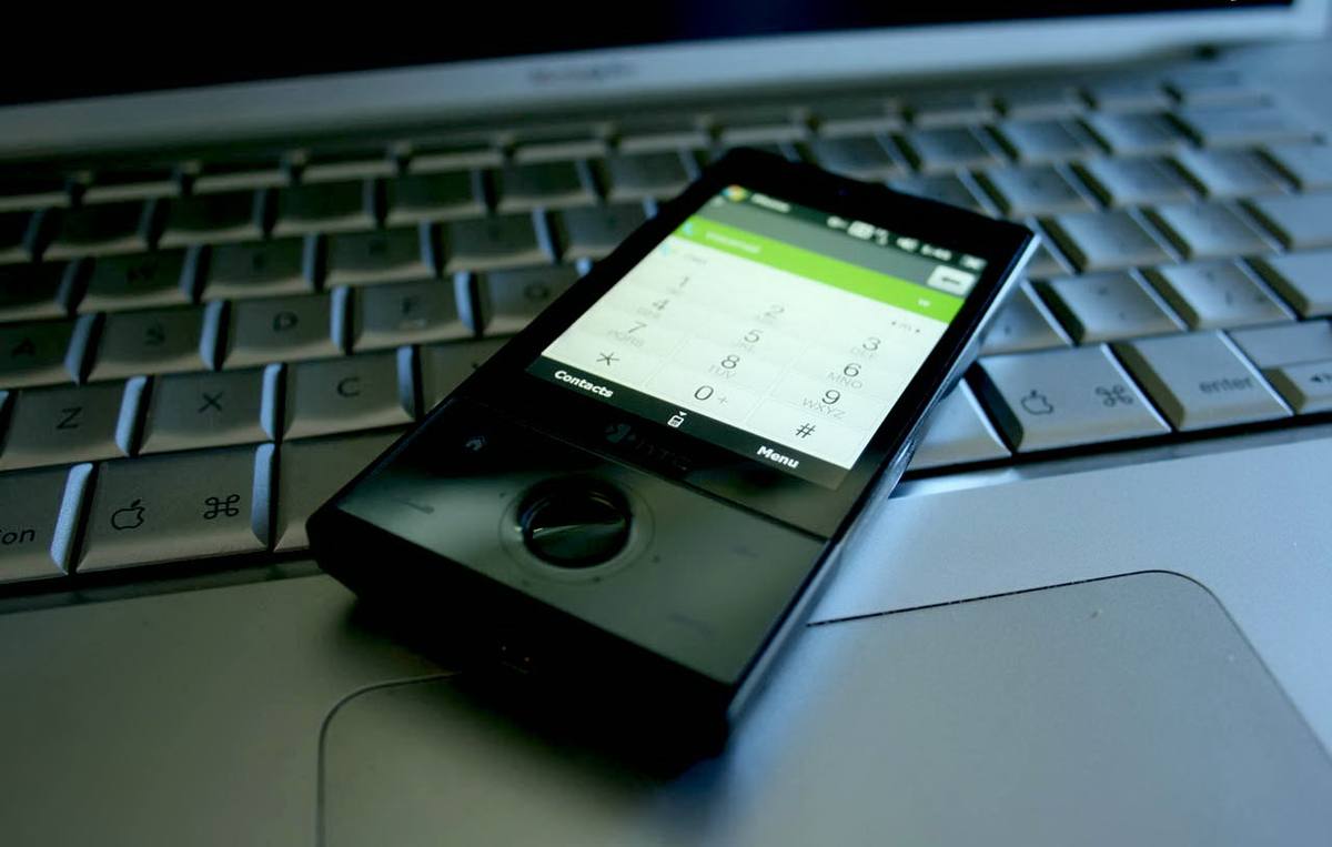 Telefon HTC Touch Diamond se zapnutým displejem leží na klávesnici notebooku
