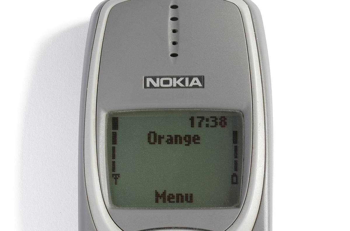 Horní část šedé Nokie 3310 s rozsvíceným displejem, na kterém stojí jméno operátora a položka Menu