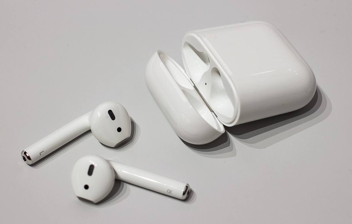 Bílá sluchátka AirPods první generace ležící vedle otevřeného nabíjecího pouzdra