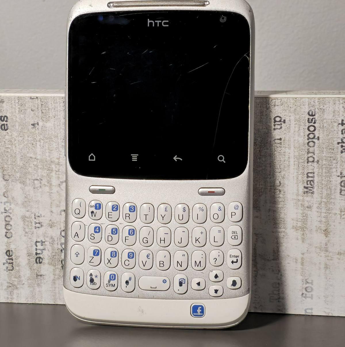 Bílý telefon HTC ChaCha s hmatovou klávesnicí a modrým tlačítkem Facebooku pod ní