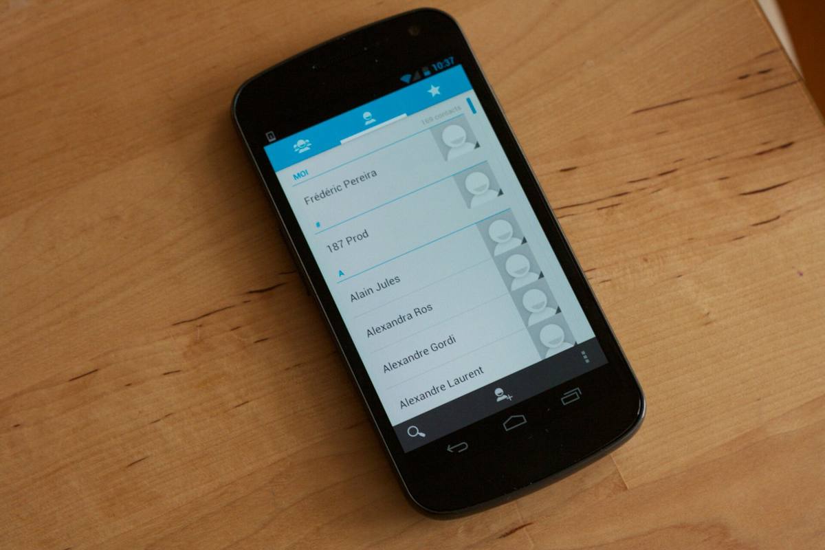 Samsung Galaxy Nexus leží displejem vzhůru na dřevěném stole, na obrazovce je seznam kontaktů