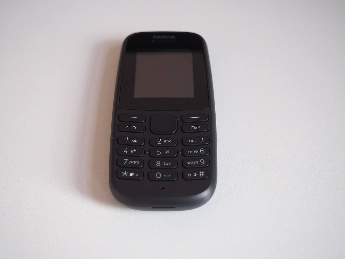 Tlačítkový telefon Nokia 105 s klávesnicí a malým displejem leží na světlé desce